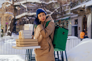 Caucasian delivery man with green backpack bringing different takeaway food in variety of paper takeout containers. Male courier carries pizza, Chinese noodles, hamburgers and coffee.