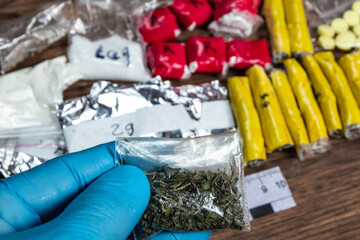 Obraz na płótnie Canvas evidence of smuggling traffic: Packaging of a narcotic substance in the hand of a forensic expert against the background of other arrested materials, cocaine, heroin, spice
