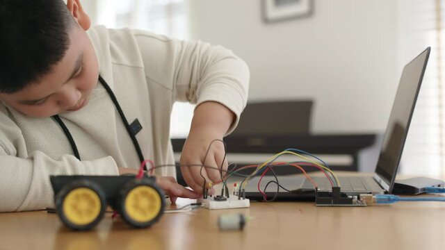 Young asia student remotely learn online at home in coding robot car and electronic board cable in STEM, STEAM, mathematics engineering science technology computer code in robotics for kids concept.
