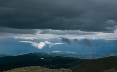 Colorado Rocky Mountain vista of low hanging clouds against a dark sky above a highlighted mountain top and lake as viewed from Mount Evans Highway, Colorado USA