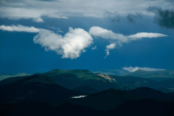 Colorado Rocky Mountain scenic of low hanging clouds against a dark sky above a highlighted mountain top and lake as viewed from Mt. Evans Highway, the highest paved road in the USA. Colorado