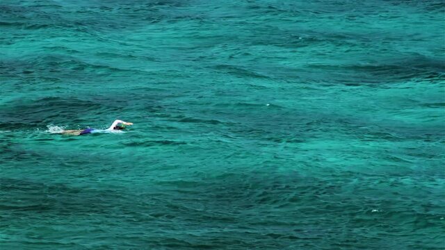 A swimmer swims in turquoise water near the island of Apo, Philippines