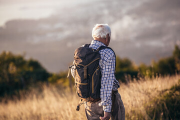 Happy old man just reaches the top of hill.Handsome senior man hiking, exploring.
