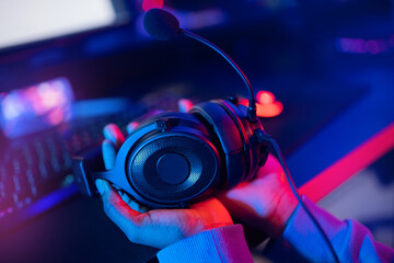 Fototapeta na wymiar Headphones with microphone in hands of young african happy woman professional gamer online video game, neon background