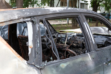 Fragment of an abandoned car damaged by fire. Vehicle has no windows and completely burnt-out interior. Side view, selective focus