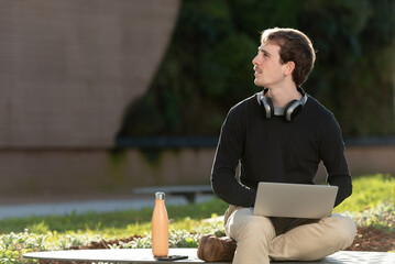 Obraz premium Handsome freelancer working on his laptop outdoors, sitting on a bench in the park with beautiful sunlight