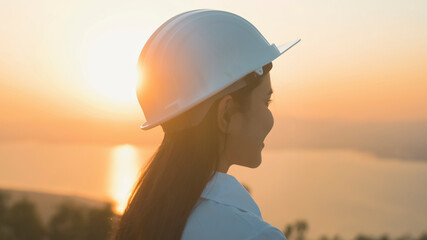 a woman engineer is putting a protective helmet on her head at sunset.
