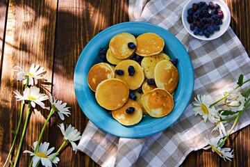 Mini pancakes with honeysuckle on a blue plate on a brown wooden background.