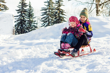 Two girls have fun on a winter walk and enjoy sledding for children. 