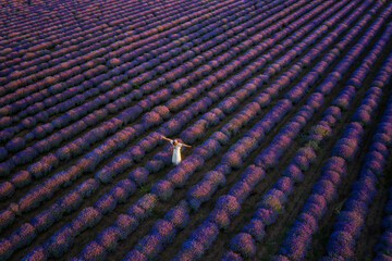 Aerial view of a woman in a white dress, among blooming lavender field at sunset