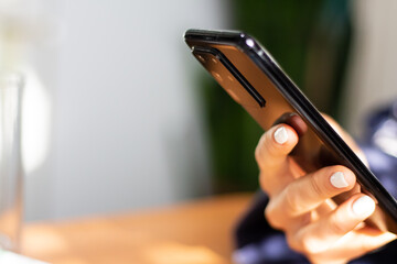 modern smartphone in black in the hands of a girl with a light manicure and rings on her finger in daylight with a place for an inscription