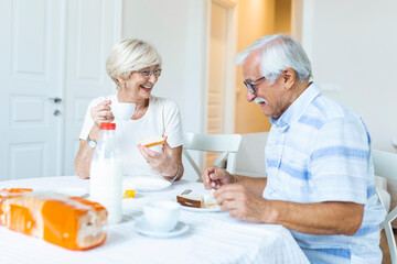 Fototapeta na wymiar Happy senior couple having breakfast at home. Elderly couple smiling to each other. Old couple having fun during breakfast. Food, eating, people and healthy food concept