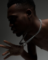 Portrait of an African man man on dark background in studio. Dark-skinned guy holding chain.