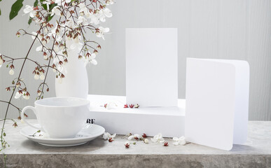 Mock up white  invitation card ,coffee cup,book  and beautiful Nodding Clerodendron flowers in modern vase set on concrete table with white wood background,greeting card in soft tone still life
