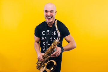 Fototapeta premium A man holding a saxophone in the studio against a yellow background