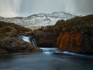 Obraz premium turquoise and idilyc water with rocks and silky water. red cliff and wintes mountains - Fairy Pools - Skye Island - Scotland - Uk