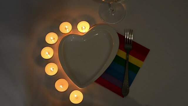 romantic snake concept. there is a plate in the shape of a heart, a glass for wine and an LGBT oak napkin for dinner, the table is decorated with lights and candles