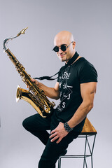 Fototapeta na wymiar Man with sunglasses and saxophone in hand, in studio on gray background