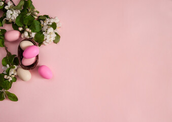 Easter composition. A border of flowering apple branches and pink-and-white eggs on a pastel pink background. Happy Easter Holidays. Top view. Free space.