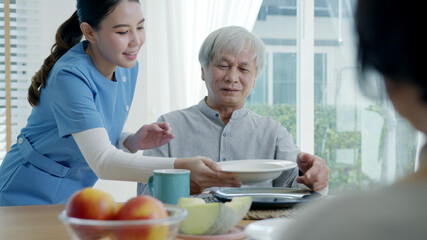 Attractive young senior asian citizen couple happy sit, talk, eat soup for healthy nutrition breakfast meal on dining table at home in morning in routine lifestyle in old asia nursing in-home care.