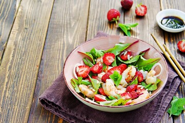 Salad with fresh strawberries, fried shrimp and young beet tops in a pink bowl