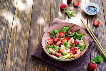 Salad with fresh strawberries, fried shrimp and young beet tops in a pink bowl
