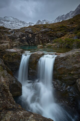 Fototapeta na wymiar vertical long double cascade with turquoise water between idyllic landscape of mountains with snow- Fairy Pools - Skye Island - Scotland - Uk