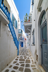 Traditional narrow cobbled streets, beautiful alleyways of Greek island town. Whitewashed houses, flower pots, blue balconies, stairs. Mykonos, Greece