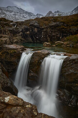 panoramic double cascade with turquoise water between idyllic landscape of mountains with snow- Fairy Pools - Skye Island - Scotland - Uk