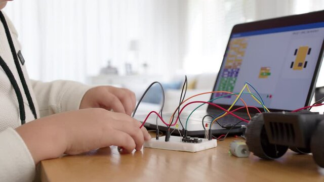 Young asia student remotely learn online at home in coding robot car and electronic board cable in STEM, STEAM, mathematics engineering science technology computer code in robotics for kids concept.