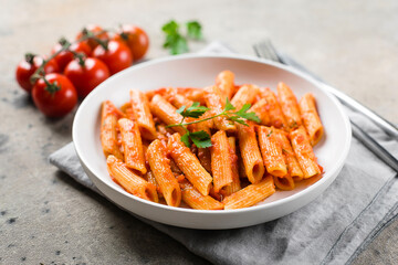 Penne pasta with tomato sause in white plate on stone background table. Closeup. Italian food