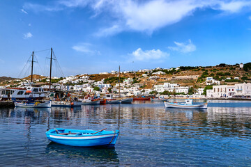 Beautiful summer in marina of Greek island. Fishing boats, yachts moored at jetty. Whitewashed houses. Small blue boat in foreground. Mykonos, Greece.