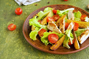 Warm salad with fried chicken fillet, lettuce and cherry tomatoes on a brown clay plate on an olive concrete background.
