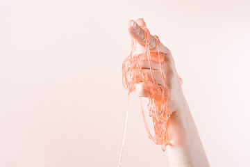 Slime flows down the index finger of the woman's hand on a light beige background