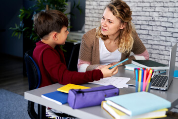 Fototapeta premium Smiling mother explains to her son how to do the homework