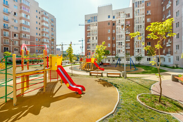 New modern colorful children playground in sunny summer green courtyard among residential high-rise buildings