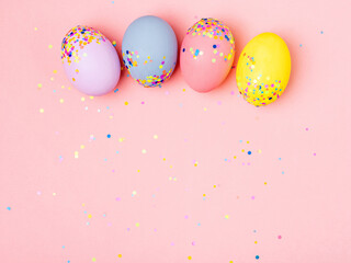 Fototapeta na wymiar Row of colourful easter eggs on trendy pink pastel background. Hand-drawn easter eggs with scattered confetti. Flat lay style. Spring holiday background.