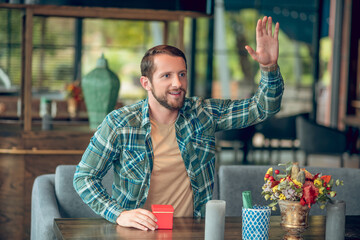 Man raising his hand at table in cafe