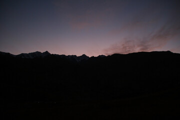 A bright orange sunset over sharp black Pamir mountains in the shade