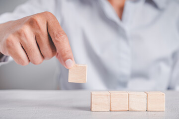 Businessman wearing a blue shirt, arranging the empty wooden blocks with his hands. Which is placed on a white wooden table. Business strategy and action plan. Copy space.