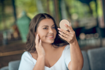 Woman holding small round mirror in outstretched hand