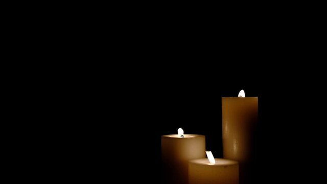 Three white candles burning. Isolated candles burning over dark background.White paraffin candles with yellow shades burns on a black background.