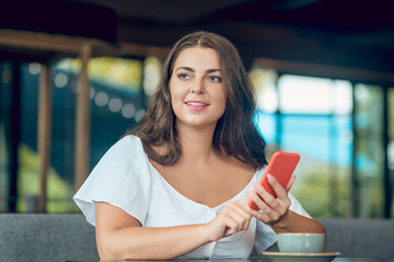 Pretty woman with smartphone pensively looking away