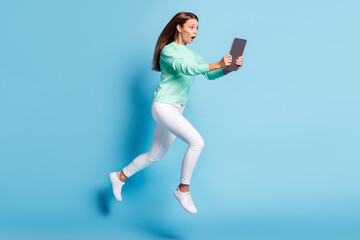 Full length profile photo of attractive student girl dressed casual sweater jumping running holding e-reader isolated blue color background