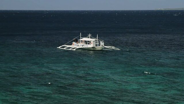 Snow-white diver boat swaying on sky-blue water under the coral reef on the Apo Island, Philippines