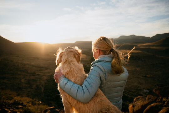 Caucasian young teen hugging golden puppy while gazing into horizon during vibrant sunset 