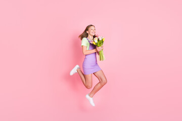 Full length body size photo of little girl jumping with tulips bunch laughing happy isolated pastel pink color background