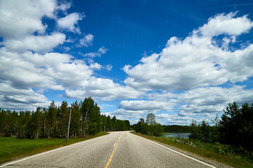 View from relief car windscreen on the blue sky with white clouds, grey asphalt road and landscape with forest and green teeses. Landscape through window