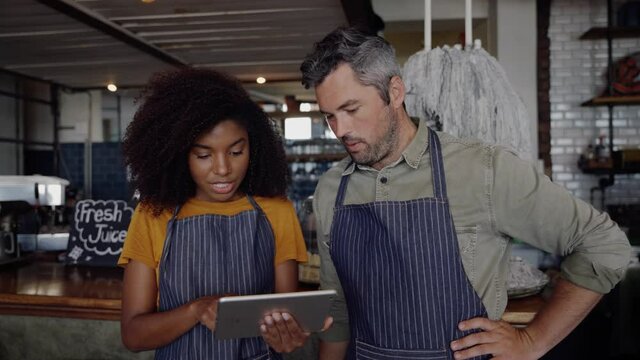 Waiter and waitress attempting to workout online menu on digital tablet while standing in trendy cafe