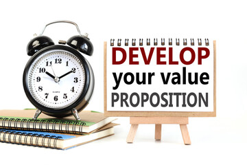 Develop your value proposition. text on white notepad paper on a stand next to our desk clock on a sideboard. on white background